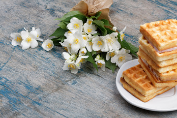 A stack of Belgian waffles on a white plate, on a wooden painted background. Bouquet of jasmine flowers. Spring romantic breakfast.