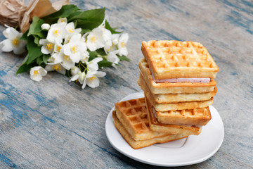 A stack of Belgian waffles on a white plate, on a wooden painted background. Bouquet of jasmine flowers. Spring romantic breakfast.