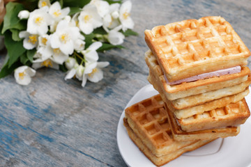A stack of Belgian waffles on a white plate, on a wooden painted background. Bouquet of jasmine flowers. Spring romantic breakfast.