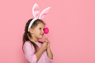 Obraz na płótnie Canvas Portrait of cute little child girl with Easter bunny ears holding colorful eggs on pink background. Happy easter