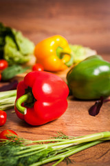 Red, green and yellow peppers and other vegetables on a brown wooden background.