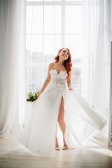 Happy bride in white wedding dress swirls near large window