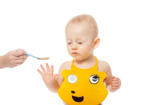 little blond boy not want to eat a porridge with a spoon. Boy from frustration and reluctance is pushes away with his hands. Isolated on white background
