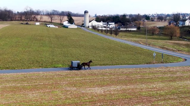 Aerial a traditional Amish horse and buggy travels down the road to an intersection makes a hard right to continue the journey down the roadway.