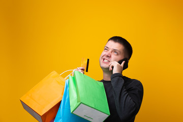 Photo of male shopper with paper bags, bank card and phone in hand