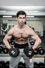 Fototapeta na wymiar Athletic man in gym working with dumbbells