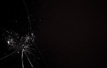 A shattered glass on a black surface, with many sharp shards forming a white irregular textured...
