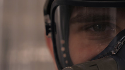 In slow motion a professional man (guy) in a garage (service) in working clothes dressed in a sweater sets up a paint gun (spray gun) and starts painting (putting a layer of ceramics) a yacht.