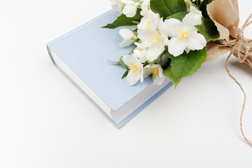 Obraz na płótnie Canvas Closed book and jasmine flowers. A bouquet of flowers on a blue book on a white background.