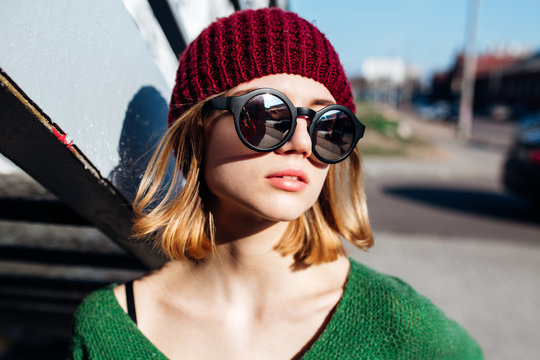Close up image of happy brunette woman in sunglasses and knitted clothes posing sideways outdoors