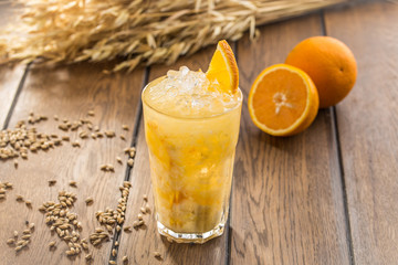 fresh squeeze natural orange juice in clear drinking glass and wheat spikes on wooden table