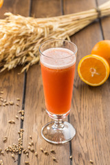 Carrot juice in glass and fresh orange and wheat spikes on wooden table