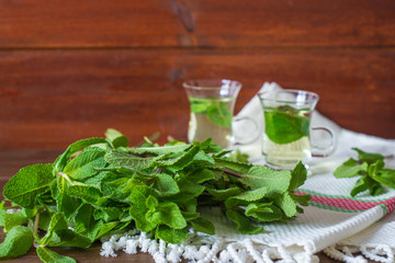 Mentha leafs with small glass tea cups on behind  on wooden background 