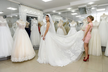 Naklejka premium Wedding consultant helps bride fit wedding dress in salon
