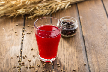 Red Berry Juice in Glass and wheat spikes on wooden table