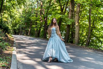 Fototapeta premium Girl in dress on the summer road between trees