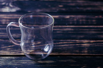 Empty glass cup on the dark wooden table and black background