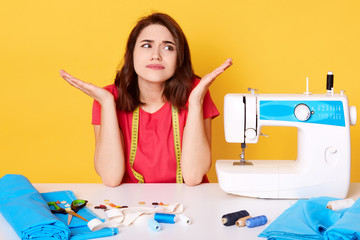 Studio shot of tsylist girl artisan seamstress sitting at white desk with sewing machine, stitch,...