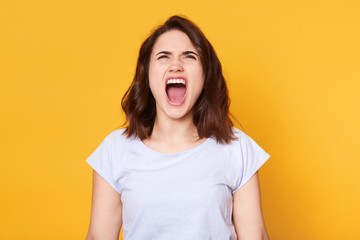 Screaming emotional angry woman poses isplated over yellow studio background, quarrels with her husband. Young female half length portrait. Human emotions, facial expression concept. Copy space.