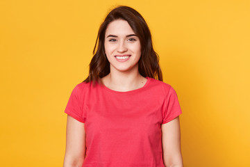 Fototapeta premium Close up portrait of young woman showing smile, dressed casual clothing, isolated against yellow background, being in good mood, looks directly at camera, has pleasent facial expresion. Copy space.