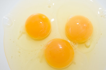 Three broken chicken eggs in a white mixing bowl