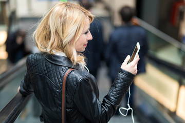 Young blonde woman using her smartphone on an escalator in the subway