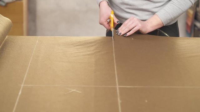 A tailor cutting a high quality brown fabric using professional scissors
