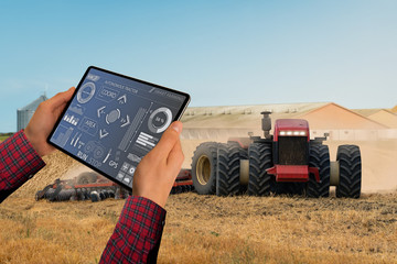 A farmer with digital tablet controls an autonomous tractor on a smart farm