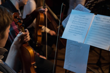 Symphonic violin orchestra plays classical music in pit. Music stands with notes. 