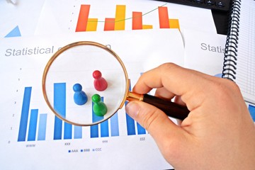 A young man is holding a magnifying glass in his hand, looking at statistic figures - a business concept on the subject of sampling and selecting the right target group and examining it