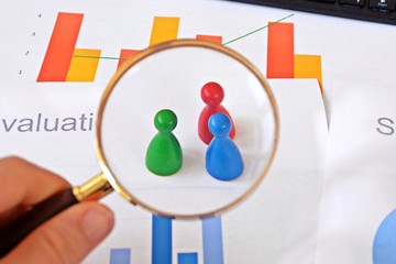 A young man is holding a magnifying glass in his hand, looking at statistic figures - a business concept on the subject of sampling and selecting the right target group and examining it
