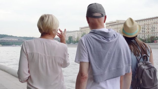 Back view of happy family having great time enjoying summer vacation together in Moscow, Russia. Senior couple with young teenage daughter walking along promenade in Gorky Park laughing and chatting