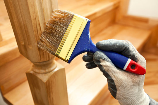 Painter paints a varnish wooden board by brush