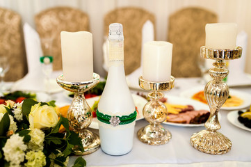 Festive table for guests, decorated with white candles, a bottle and the bouquet of flowers. Wedding banquet.
