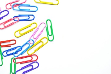 Various colored paper clips lie across a white surface - a background consisting of a white base and colorful paperclips