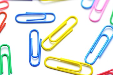 Various colored paper clips lie across a white surface - a background consisting of a white base and colorful paperclips