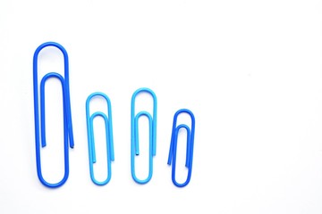 Various colored paper clips lie across a white surface - a background consisting of a white base and colorful paperclips