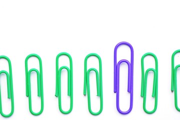 Various colored paper clips lie across a white surface - a background consisting of a white base and colorful paperclips