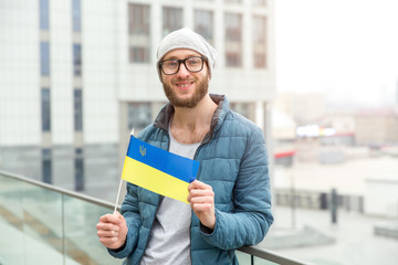 Young man in glasses with Ukraine flag on city background.