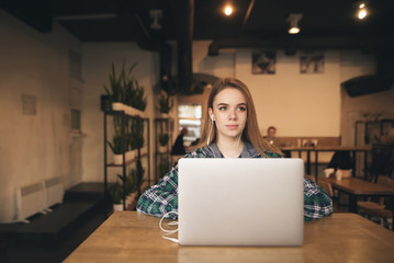 Attractive girl with headphones and casual clothes is working on a laptop in the cafe. Freelance girl sits in a cozy coffee shop with a laptop