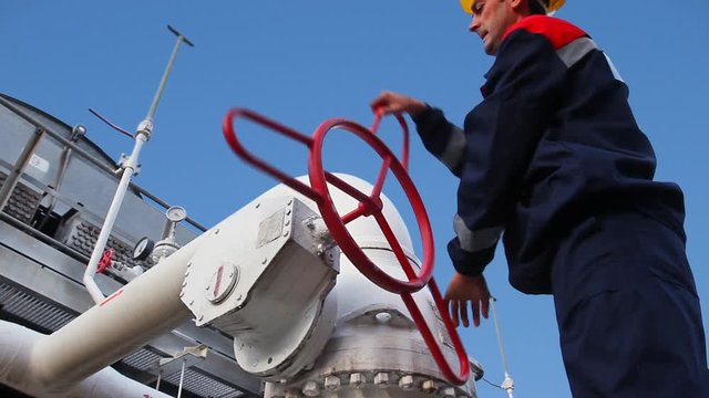 worker closes ball valve on cooling installations at gas compressor station, against background of blue sky, closeup