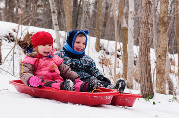 Brother and sisters (5 and 3 yrs old) sledging together in Quebec in winter