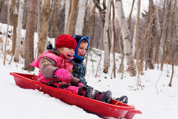 Brother and sisters (5 and 3 yrs old) sledging together in Quebec in winter