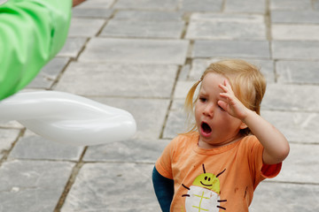 A little girl (3 yrs old) yawning while she watches a balloon sculptor making a balloon.