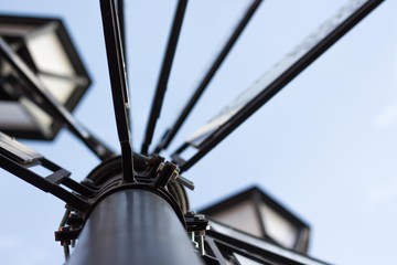 The lamp post is made of metal against a blue sky with signboards of cities. In the daytime lights...
