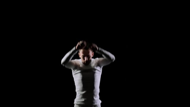Young handsome male acrobat gymnast in white clothes on a black background makes jumps and shows tricks with rotation and somersault on a trampoline in slow motion