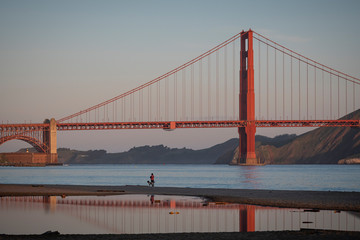 Golden Gate bridge, early morning.  Woman walking a dog on the beach in foreground.