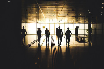 Group of people walking in the train airport gate station to move and travel for job or leisure - sunny backlight in background - dark and black tones