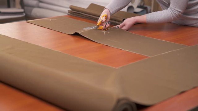 A tailor cutting a high quality brown material using professional scissors and squaring cut pieces
