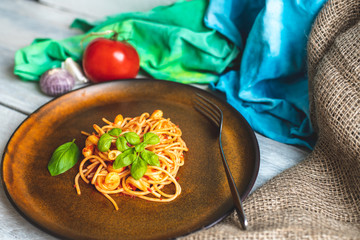 on a white, wooden, rustic kitchen table lies a plate with a small portion of spaghetti in tomato sauce, with oregano and fresh basil leaves